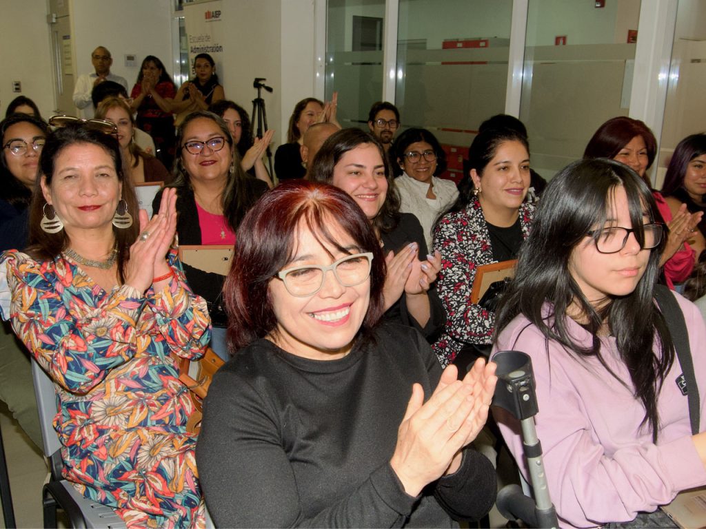 Asistentes sonrientes, predominantemente mujeres, aplaudiendo sentados en un auditorio durante un evento académico o institucional.